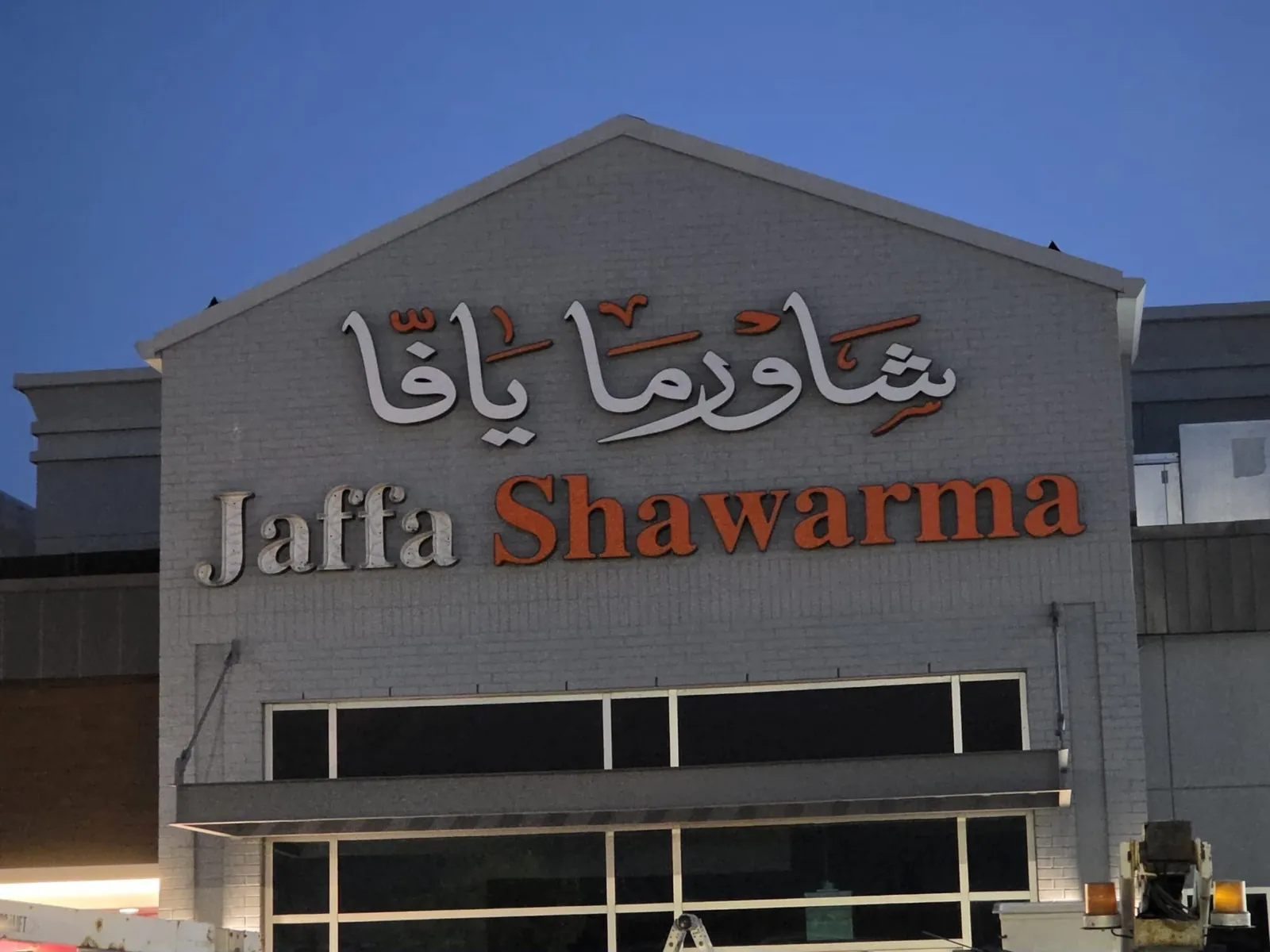 Jaffa Shawarma dimensional letters and Arabic calligraphy on a grey gable at dusk