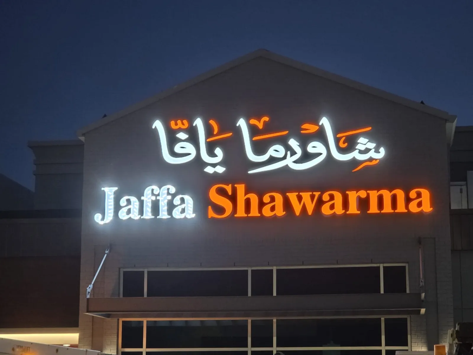 Jaffa Shawarma illuminated Arabic and English channel letters glowing white and orange at night