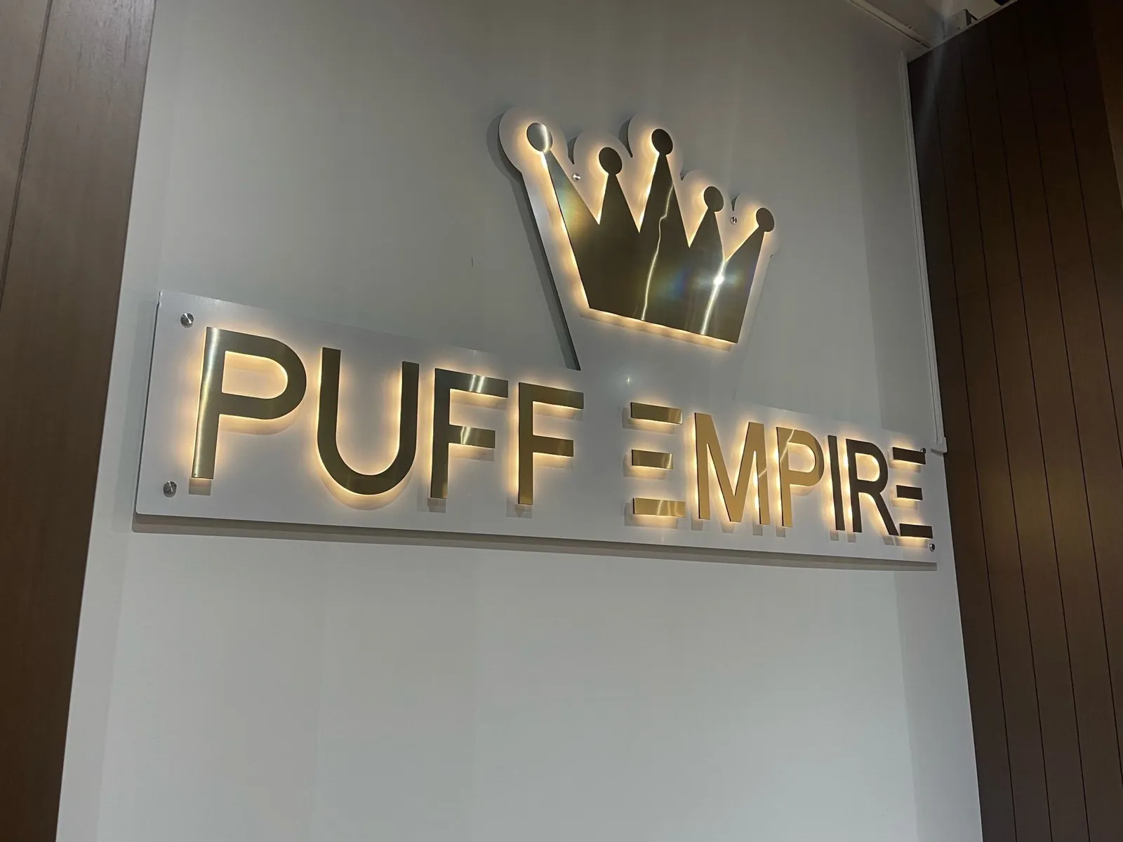 Puff Empire halo lit brushed gold letters and crown on an acrylic panel